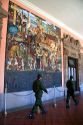 Men in military uniform walk past a mural painted by Diego Rivera at the National Palace in Mexico City, Mexico.