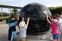 Children push the Constellation Sphere, a 9 ton granite sphere floating on water at the Kennedy Space Center Visitor Complex in Cape Canaveral, Florida.