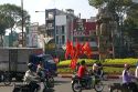 Vietnamese people ride motorbikes past Kentucky Fried Chicken sign and communist flags in Ho Chi Minh City, Vietnam.