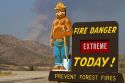 Smokey Bear extreme fire danger sign with a plume of smoke from a forest fire in the back ground in Boise County, Idaho, USA.