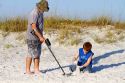 Father and son using a metal detector at the beach on the gulf coast of Florida, USA.
