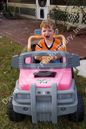 A three year old boy driving a battery powered car. MR