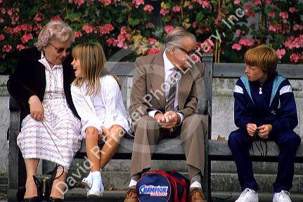 Grandparents visit with their grandchildren on a park bench in London, England.