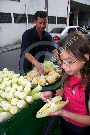 A young girl eating a corn snack she bought from a street vendor in the Liberdade asian section of Sao Paulo, Brazil.
