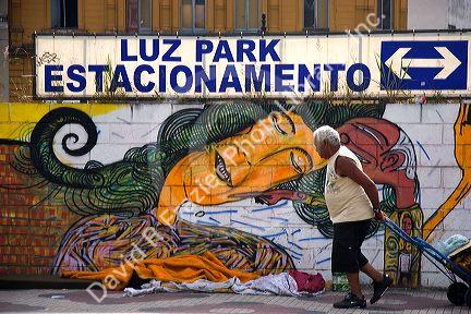 An elderly woman walking past a subway station painted with grafitti in Sao Paulo, Brazil.