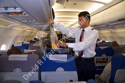 A male flight attendent conducting saftey demonstration of the use of the oxygen mask.