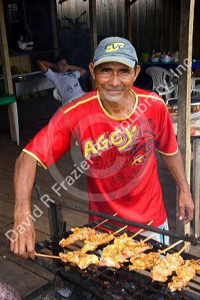 Brazilian man cooking chicken on a grill at a village in the Amazon, Brazil.
