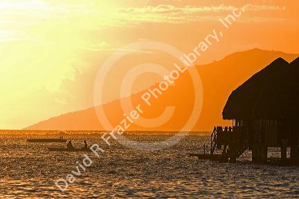 Grass hut bungalow and boats at sunset on the island of Tahiti.