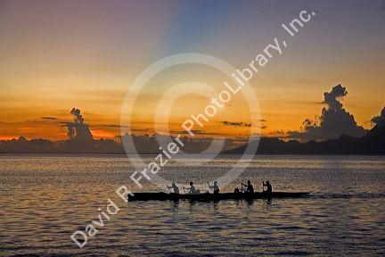 Outrigger canoeing at sunset off the island of Tahiti. The blue band in the sky is believed to be the shadow cast from a mountain on a distant island.