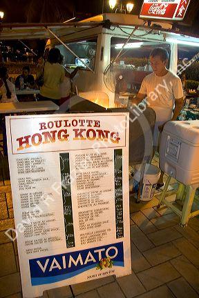 The menu board and cook for a roulotte, food van in Papeete on the island of Tahiti.