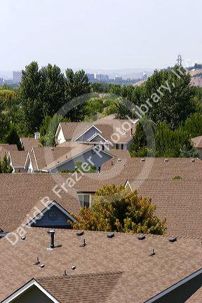 Rooftops of suburban sprawl housing with smog over the city of Boise, Idaho in the background.