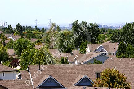 Rooftops of suburban sprawl housing with smog over the city of Boise, Idaho in the background.