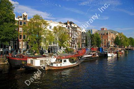 Row houses and canal boats on the Amstel River in Amsterdam, Netherlands.