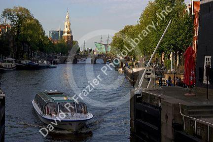 Canal boat on the Amstel River with the Montelbaans Tower in the background, Amsterdam, Netherlands.