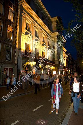 People walking on the street in front of the Royal Carre Theatre at night in Amsterdam, Netherlands.