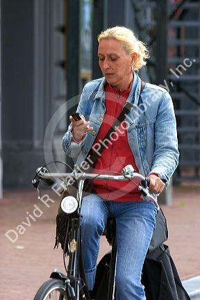 Woman using a cell phone while riding a bicycle in Amsterdam, Netherlands.