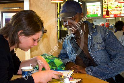 Black male and French girl check a bus schedule at a fast food restaurant in Cherbourg-Octeville in the region of Basse-Normandie, France.