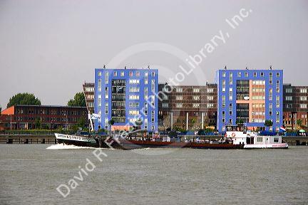 A barge on the Nieuwe Maas river at Rotterdam, Netherlands with modern apartment buildings in the background.