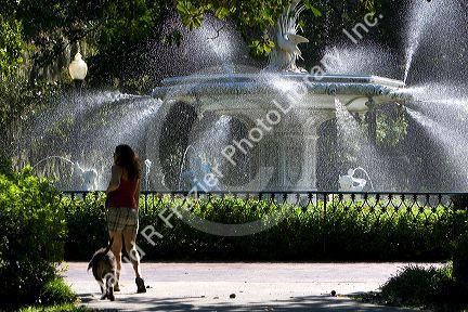 Woman walking her dog near a large water fountain in Forsyth Park in the historic district of Savannah, Georgia.