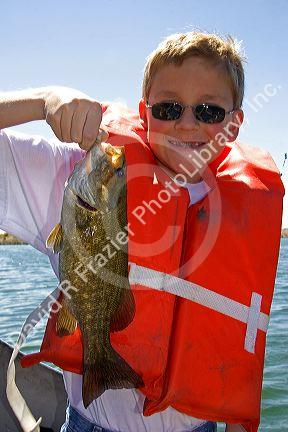 A twelve year old boy wearing a life jacket and holding a bass he caught while fishing in Idaho. MR