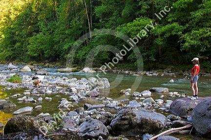 A woman walks her dog along a river in the Swiss Alps near Zurich, Switzerland.europe, european, swiss, switzerland, swiss alps, alps, travel, tourism, river, nature, dog, woman