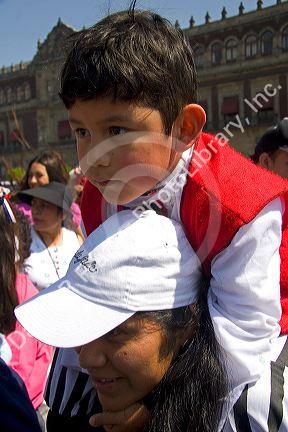A young Mexican boy sits on his mothers shoulders to see over the crowd of people celebrating the Day of the Dead in the Zocalo in Mexico City, Mexico.