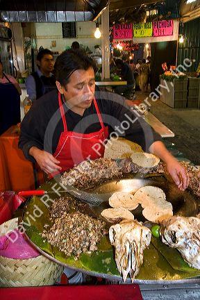 Vendor cooking cabeza tacos using a cazo at the Merced Market in Mexico City, Mexico.