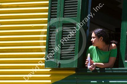 Woman looking out the window of a colorful building in the La Boca barrio of Buenos Aires, Argentina.