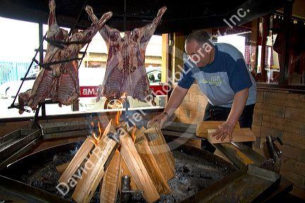 Man cooking lamb meat over an open fire in a restaurant at Ushuaia on the island of Tierra del Fuego, Argentina.