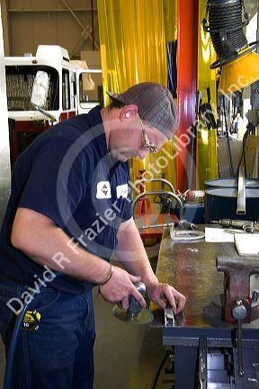 Worker using a power grinder on metal parts for a truck chassis at Spartan Motors manufacturing plant in Charlotte, Michigan.