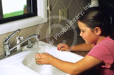 Eight year old girl getting a glass of water from the kitchen faucet.