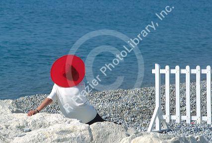 Woman sitting on the beach with a red hat along the French Riviera near Nice, France.