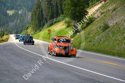 Classic American cars travel over the high mountain Teton Pass on Wyoming Highway 22 near the state border of Wyoming and Idaho.