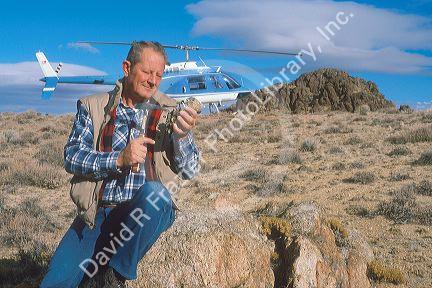 Mining engineer examines rocks with helicopter in background.