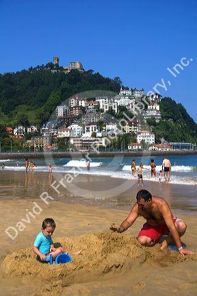 Father and son playing in the sand at La Concha Bay in the city of Donostia-San Sebastian, Guipuzcoa, Basque Country, Northern Spain.