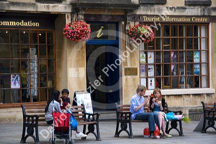People eating ice cream on park benches in front of the Tourist Information Centre in Bath, Somerset, England.