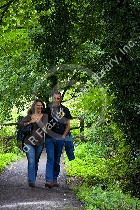 Couple walking along a tree lined path in the village of Bibury, Gloucestershire, England.