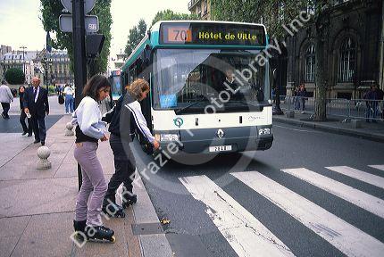 Girls crossing the street wearing rollerblades while a public bus waits in Paris, France.