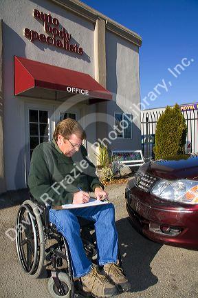 Handicapped insurance claims adjuster assessing the damage on an automobile in Boise, Idaho, USA. MR