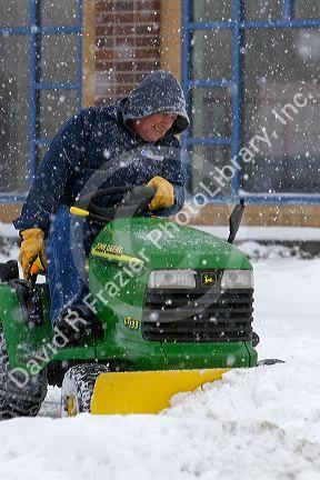 John Deere riding lawn mower fitted with a snow plow removing snow from a parking lot in Boise, Idaho, USA.