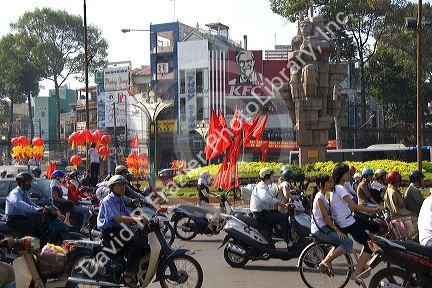 Vietnamese people ride motorbikes past Kentucky Fried Chicken sign and communist flags in Ho Chi Minh City, Vietnam.