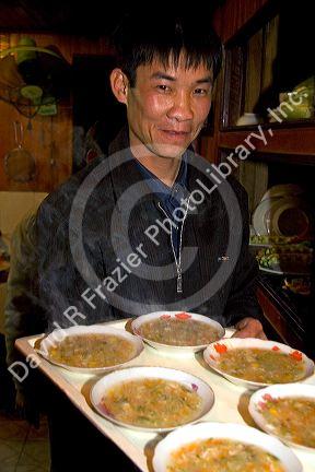 Vietnamese man serving soup to tourists on a boat in Ha Long Bay, Vietnam.