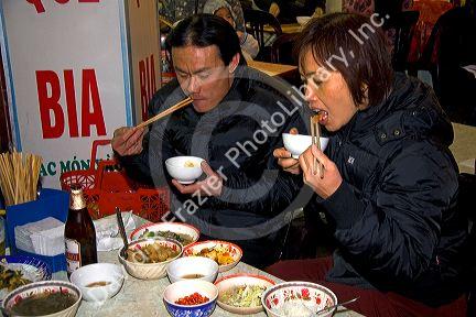 Vietnamese couple using chopsticks to eat dinner at a sidewalk cafe in Hanoi, Vietnam.