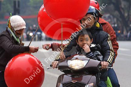 Vietnamese family on a motorbike purchase a balloon from a street vendor in Hanoi, Vietnam.