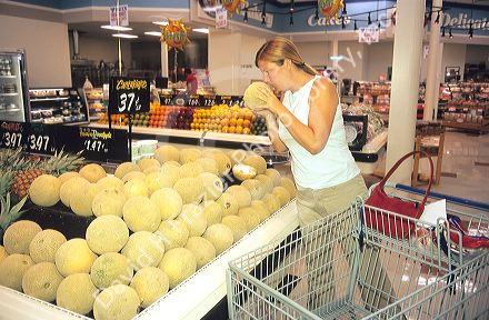 Woman shopping for cantilope in the produce section of a grocery store.