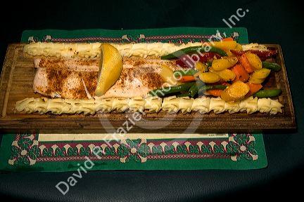Great Lakes Whitefish cooked on a wood plank searved with potatoes and vegetables at a restaurant in the Upper Peninsula of Michigan, USA.