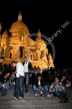 People gather on the steps of the Sacre-Coeur Basilica at night in Paris, France.