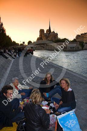 Parisiens picnicing along the River Seine at sunset in Paris, France.