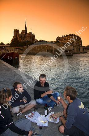 Parisiens picnicing along the River Seine at sunset in Paris, France.