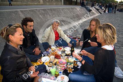 Parisiens picnicing along the River Seine at sunset in Paris, France.